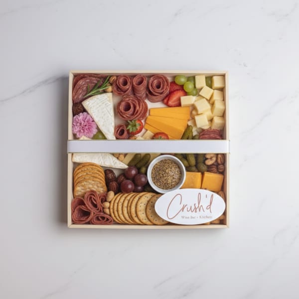 A Crush'd Wine Bar Kitchen charcuterie box with meats, cheeses, fruit, crackers, and mustard.