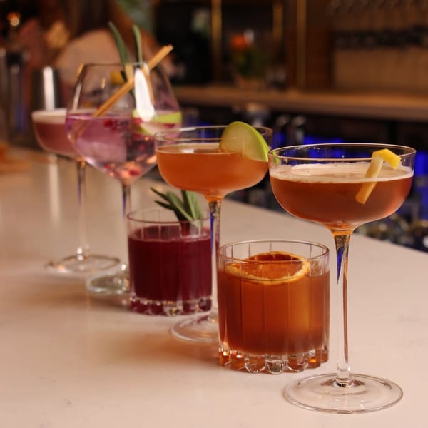 A row of five colorful cocktails with garnishes on a white bar top at Crush'd Wine Bar Kitchen.