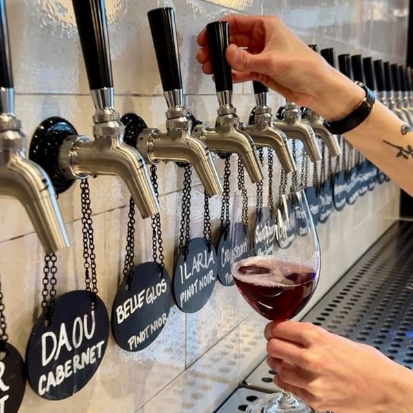 A hand pours red wine from a tap into a glass at Crush'd Wine Bar Kitchen.