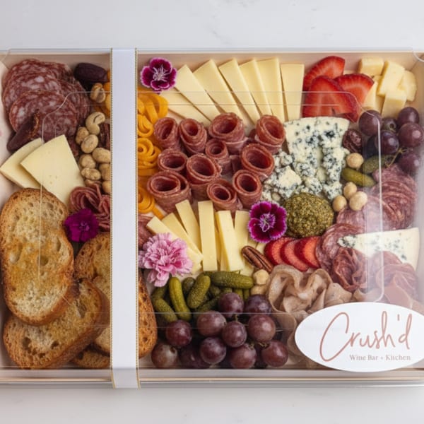 A Crush'd Wine Bar Kitchen charcuterie box filled with meats, cheeses, fruits, nuts, and crackers.