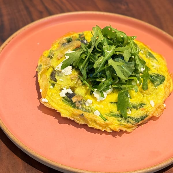 A vibrant yellow omelet topped with fresh arugula and crumbled feta cheese on a coral plate.