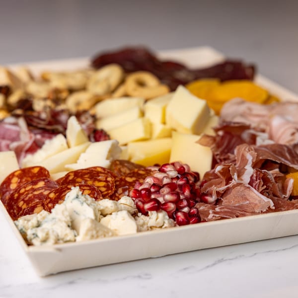 Close-up of a charcuterie board with various cheeses, cured meats, nuts, and pomegranate seeds.