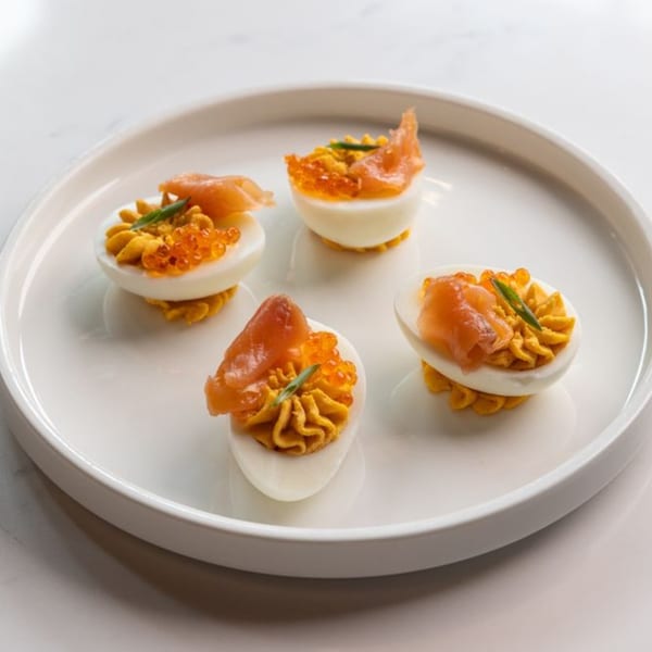 Four deviled eggs with salmon, orange roe, and green garnish on a white plate.