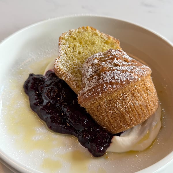 Two powdered sugar-dusted muffins with berry jam and cream in a white bowl.