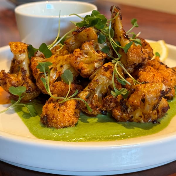 Roasted cauliflower florets with green sauce, microgreens, and a lemon wedge on a white plate.