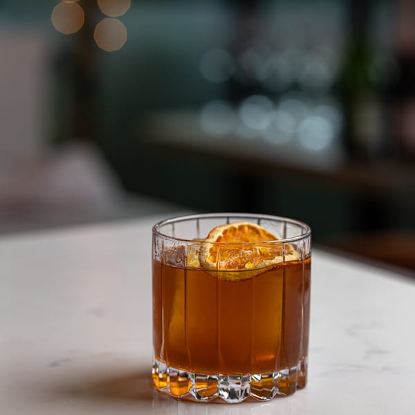 A Crush'd Wine Bar Kitchen cocktail, garnished with a dried orange slice, on a white marble bar.