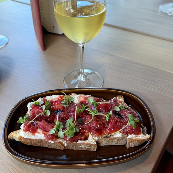 Strawberry bruschetta with cream cheese and microgreens, next to a glass of white wine.