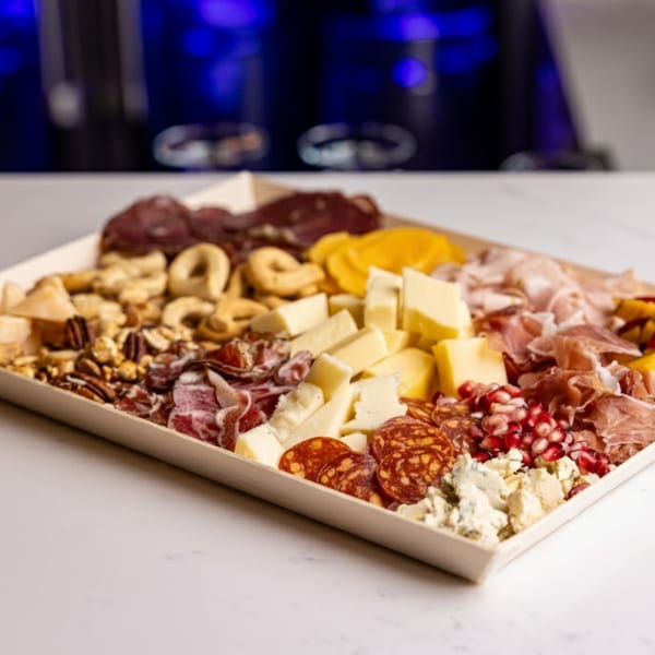 A large charcuterie board with various meats, cheeses, nuts, and pomegranate seeds.