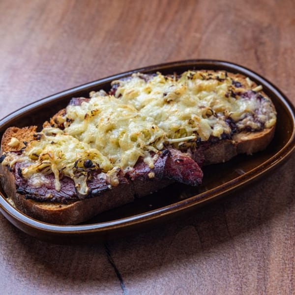Three slices of New American steak and cheese toast, topped with melted cheese and caramelized onions.