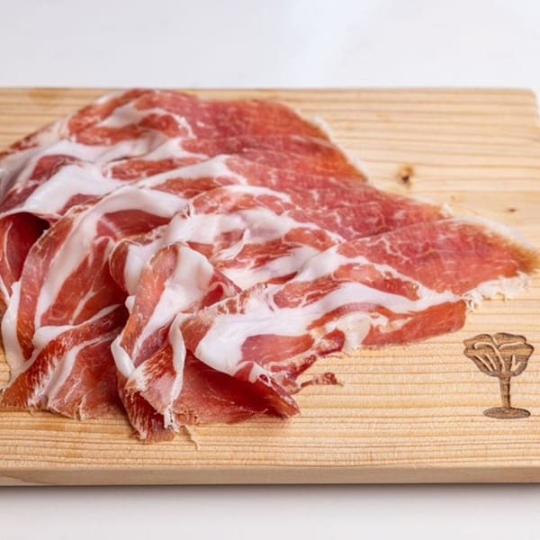 Thinly sliced prosciutto, with rich red meat and white fat, arranged on a light wooden board.
