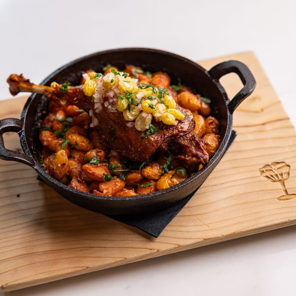 Duck confit with roasted potatoes, topped with golden raisins and diced onions, served in a cast iron skillet.